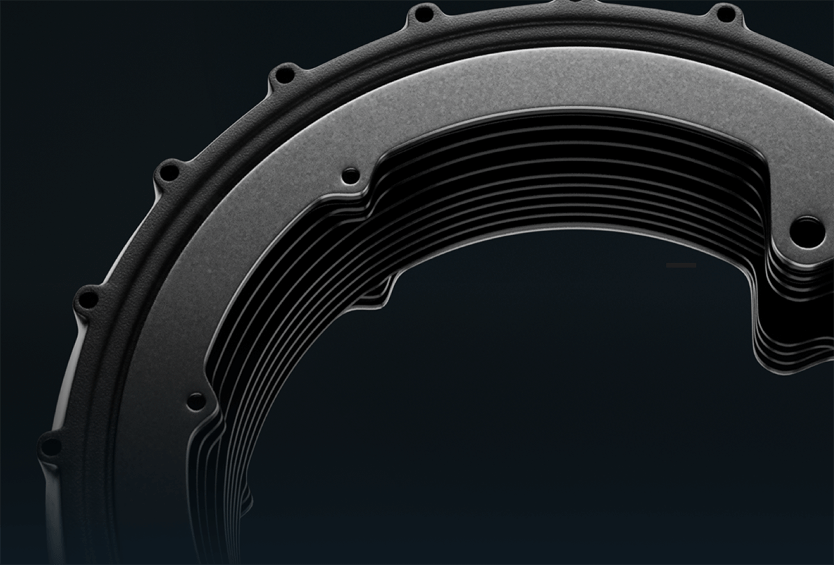 Close-up of a circular, layered metallic component with multiple screw holes, possibly part of a machine or engine, set against a dark background.